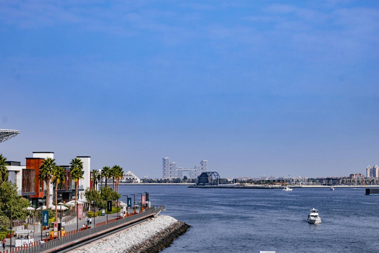 Waterfront buildings with palm trees and a calm blue sea.