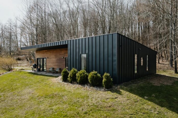 a small black cabin in the middle of a field